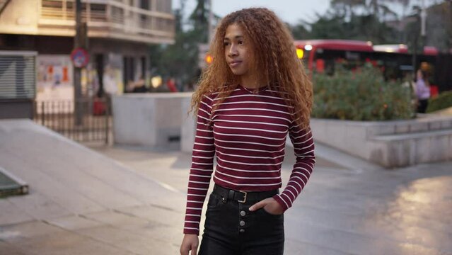 Circular motion around a young woman with curly hair. They stand with a white and maroon striped sweater