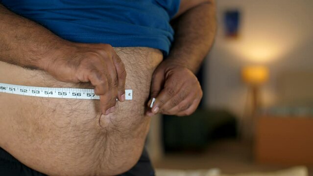 A fat man measures the size of the abdomen with a centimetre measuring tape - tummy measurement struggle  wide waist. A middle-aged man with a large belly - excess weight  unhealthy lifestyle  obes...
