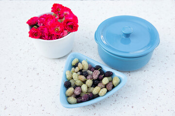 Above view of stylish bowl with berries, blue pan and cup with pink roses lying on white marble table. Concept of summer.