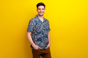 Photo of satisfied optimistic friendly man with bristle dressed blue clothes holding arms in pockets isolated on yellow color background