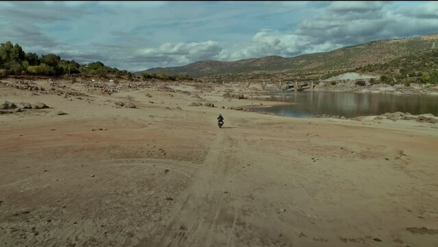 Drone shot of rider on custom off road motorcycle. Motorbike enthusiast crossing valley landscape during the day. Extreme terrain adventure or bike journey. Motorcycling alone lifestyle. 