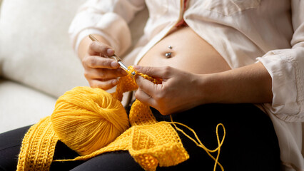 Pregnant woman knitting baby clothes. Pregnancy in the first trimester crocheting at home as a...
