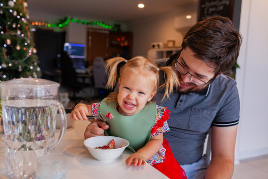 Toddler girl eating breakfast sitting on dads lap