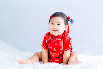 Chinese New Year concept, cute happy little girl in Chinese dress sitting in white living room. Cute Asian baby sitting in white living room, Chinese New Year concept.