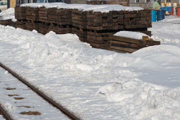 Stacks of old vintage wooden railway sleepers surrounded by snow. Tracks in foreground