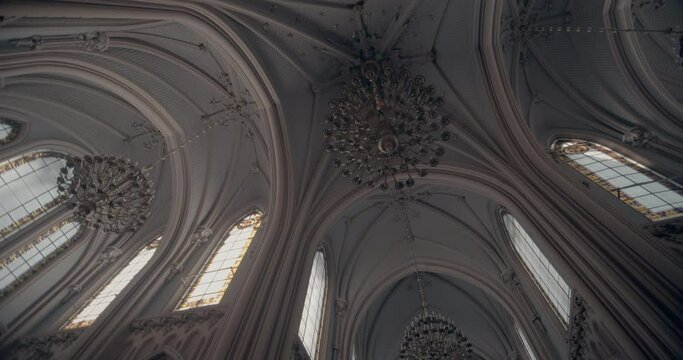 High ceiling of gothic church. High rise windows with sun rays and gothic style. Medieval style. Cathedral with vintage style. Catholic cathedral with high windows and dangling chandelier. Cold colors