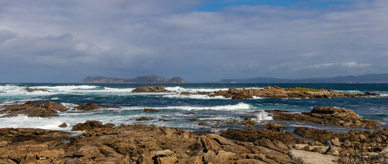Rocky coast of Galicia with lapping sea waves and the Cies Islands in the background. Spain 