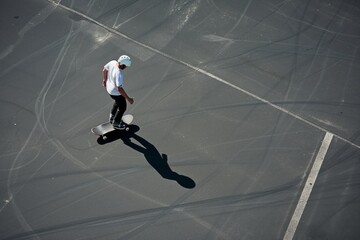 Fototapeta na wymiar solitary individual practicing skateboard tricks on empty parking asphalt