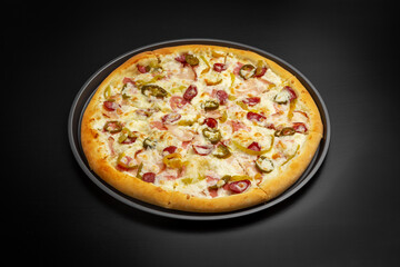Pizza with sausages, jalapenos, bacon and cheese. On a black background.