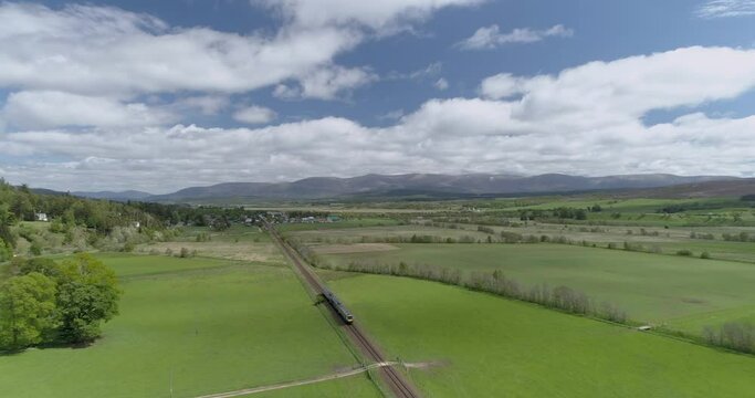 Drone view over a train passing through rural fields under a cloudy sky