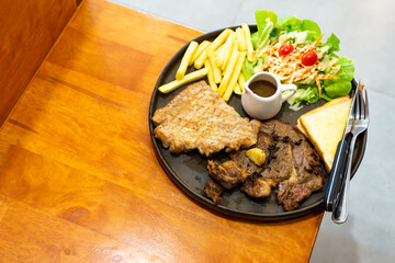 Black Pepper Pork Steak with spicy grilled chicken With salad and french fries on a black plate on a wooden table