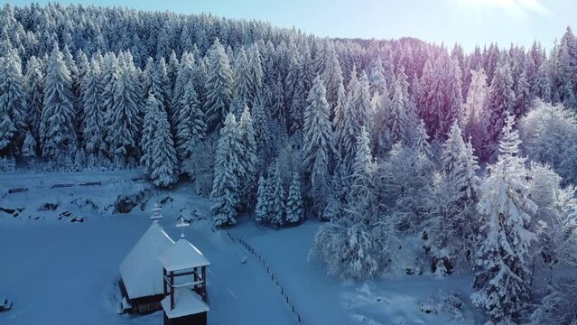Drone view of a chapel surrounded by beautiful spruces fully covered in snow on mount Trebevic