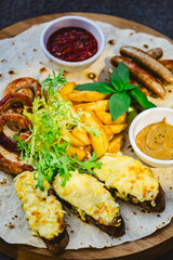 Grilled sausages with potato wedges and bread with cheese and sauces close-up on a wooden tray.