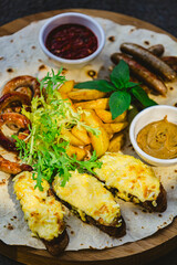 Grilled sausages with potato wedges and bread with cheese and sauces close-up on a wooden tray.