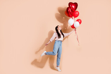 Full length photo of good mood girl wear pink shirt jeans pants fly away with balloons in hand isolated on pastel color background