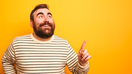 Fototapeta premium Happy Bearded Man Pointing Upwards on a Bright Yellow Background