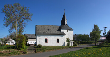 Fototapeta na wymiar Panoramic view of Krautscheid village with small medieval St. Valentin church, street and farm buildings, Eifel region in Germany