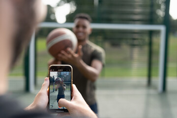 Man photographing friend with basketball ball - obrazy, fototapety, plakaty