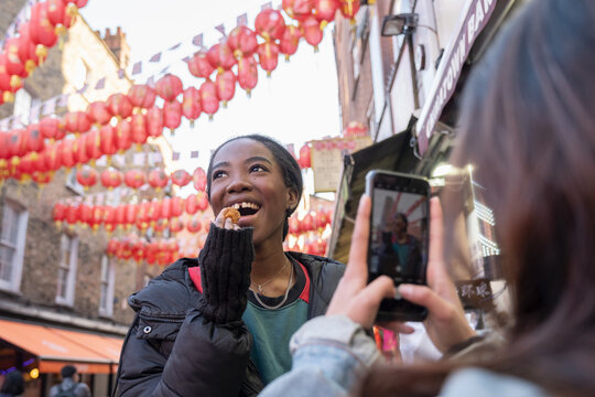 Young woman taking picture of friend eating taiyaki in Chinatown