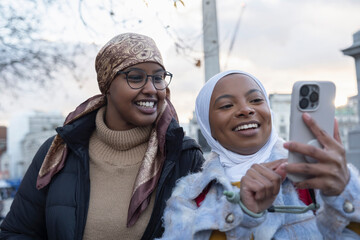 UK, London, Young female tourists in hijabs using phone in Trafalgar Square - obrazy, fototapety, plakaty