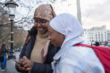 Fototapeta na wymiar UK, London, Young female tourists in hijabs using phone in Trafalgar Square