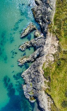 Aerial of a rocky coast of an island with sea water on one side and the forest on the island side. © Wirestock