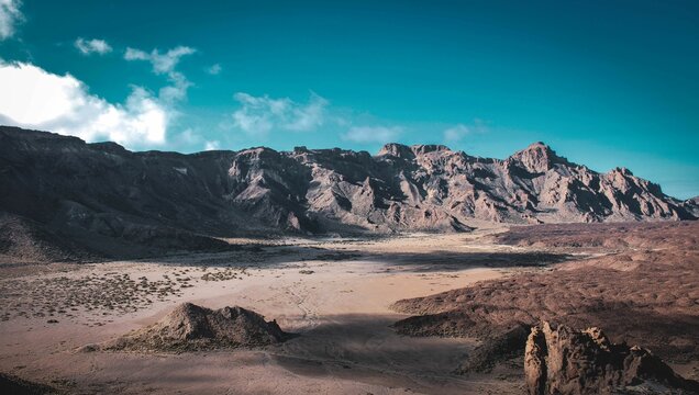 Expansive desert mountain range with dirt ground and rocky terrain.