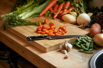 Vegetables, carrots and wood board for cooking in kitchen with onion or potato, leafy green or nutrition. Knife, garlic and counter for healthy wellness or salad diet for vegan dish, fibre or recipe