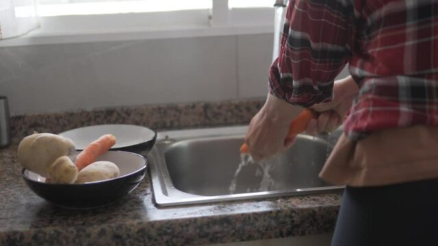 A woman cleaning carrots in kitchen sink for her dish.