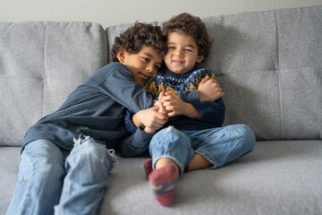 Brothers (2-3, 6-7) hugging on sofa at home