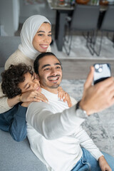 Fototapeta premium Parents and son (6-7) taking selfie on sofa at home