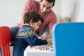 Obraz premium Father and son (2-3) coloring in coloring book at home