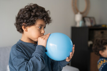 Boy (6-7) blowing blue balloon at home © Cultura Creative