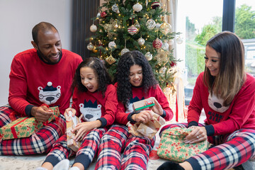 Smiling parents with two daughters unpacking gifts in front of Christmas tree