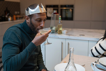 Man wearing paper crown drinking wine at Christmas dinner table