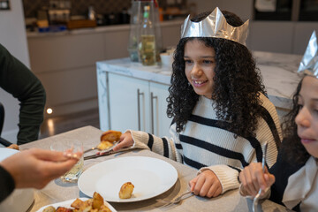 Smiling sisters in paper crowns at Christmas dinner table