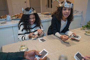Smiling girls wearing paper crowns playing cards at table