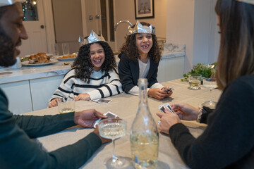 Smiling girls wearing paper crowns playing cards with parents at table