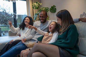 Family watching TV on sofa at home, laughing and pointing