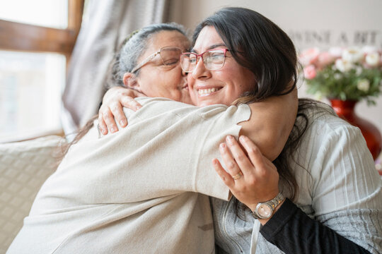 Senior mother and mature daughter hugging at home