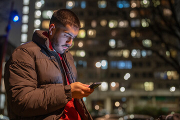 Young man using phone outdoors at night