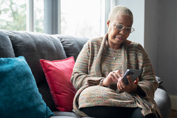 Mature woman sitting in living room with her smart phone