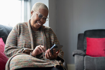 Mature woman sitting in living room with her smart phone