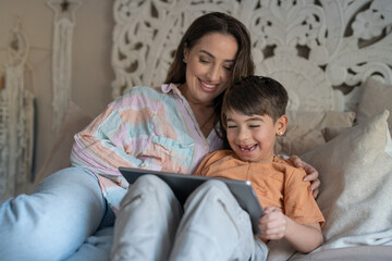 Mother and son (6-7) using digital tablet in bedroom