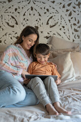 Obraz premium Mother and son (6-7) using digital tablet in bedroom