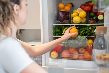 Woman opening fridge and picking fruit