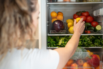 Woman opening fridge and picking fruit