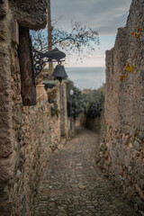 Vertical shot, a narrow, cozy medieval style street with a house ring as a bell and a beautiful sea on the background, Italy 