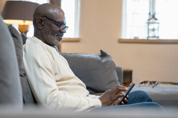 Senior man sitting on sofa and using phone