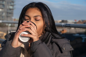 Portrait of woman in jacket drinking from disposable cup outdoors